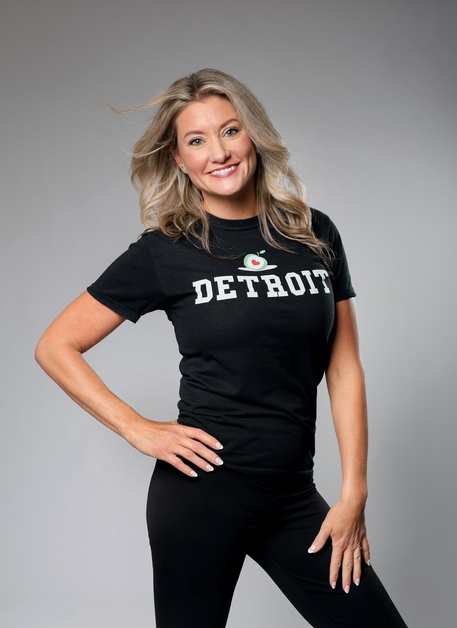 A Detroit tee and black leggings, hand on hip, on grey