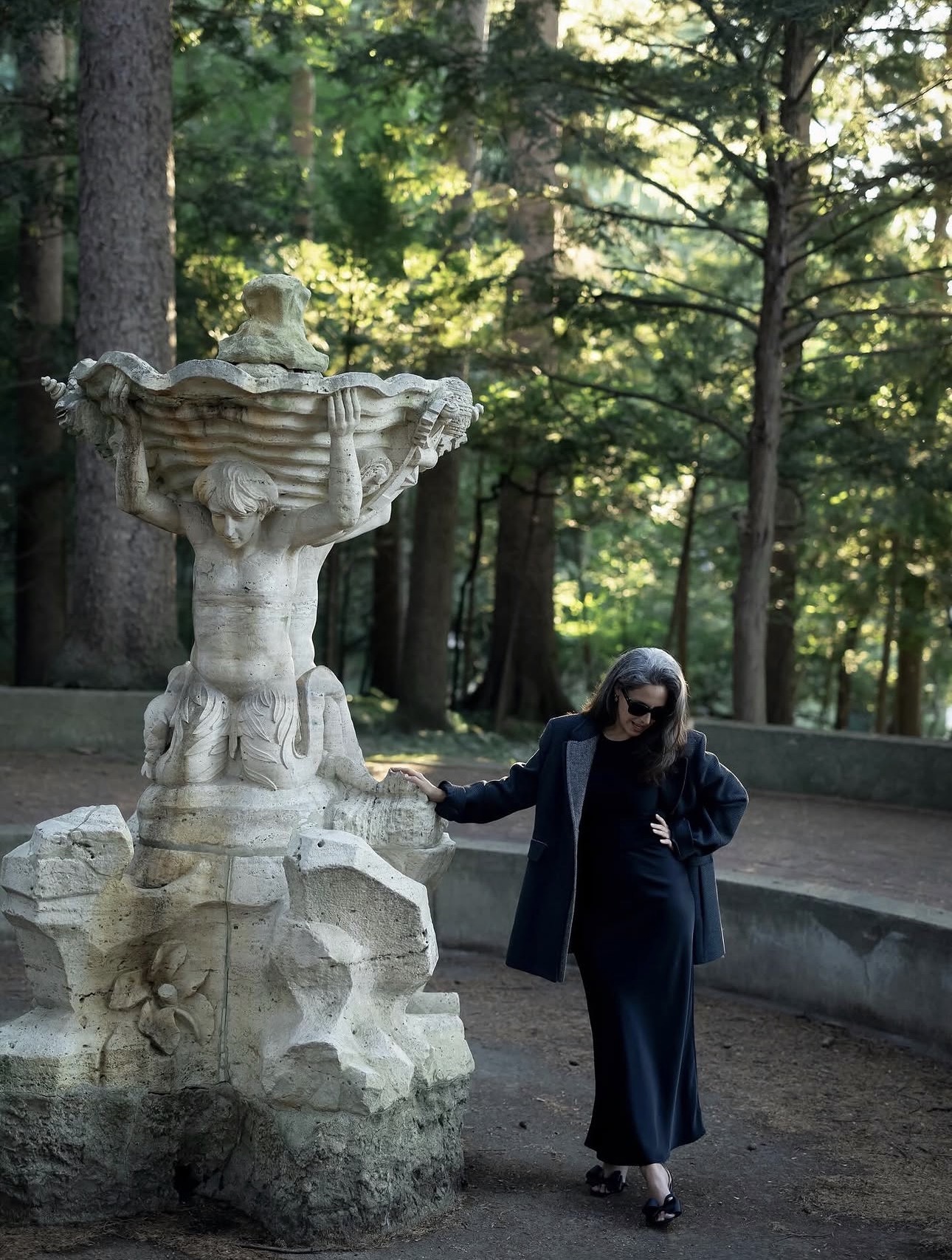 A figure beside a stone fountain in woodland