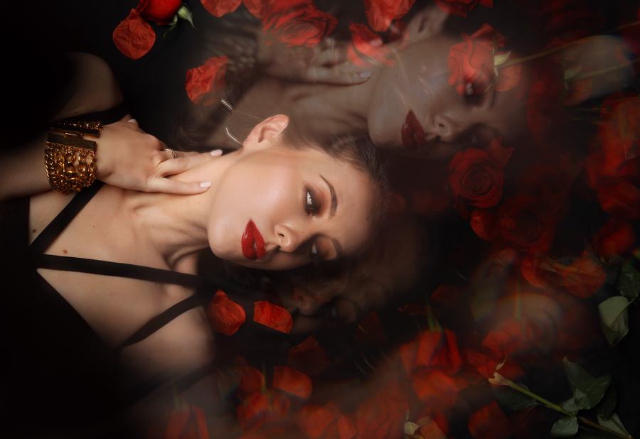 A double exposure — a face lying among red roses, mirrored above
